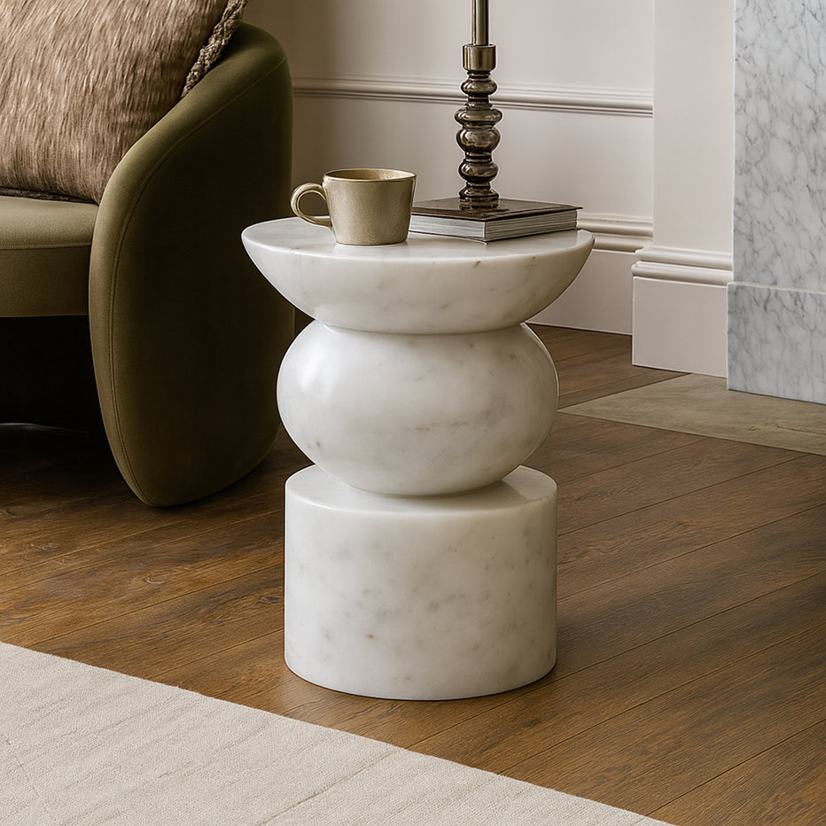 Contemporary sculptural side table featuring stacked curved forms, made from light grey marble with fine natural veins. Minimal modern interior, soft neutral tones, concrete wall background, warm wooden flooring. Professional luxury furniture photoshoot, ultra-high resolution, realistic stone texture, international design aesthetic.