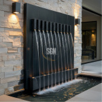 A luxury modern Black Marble Wall Fountain crafted from Bhainslana stone, featuring multiple vertical water streams cascading into an illuminated rectangular basin against a textured stone wall.